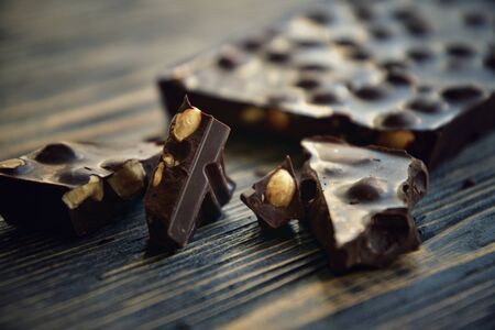 A bar of dark chocolate with hazelnuts and pieces of chocolate on a dark wooden background. Close-up. Side view.の写真素材