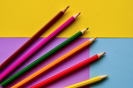 Multi-colored pencils lie on colorful sheets of paper. Bright background. Top view.の写真素材