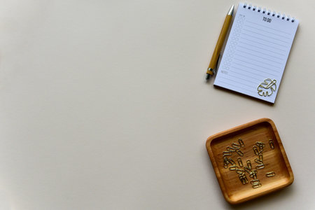 Notepad with wooden pen and wooden tray with golden staples on a beige paper background. Top view....