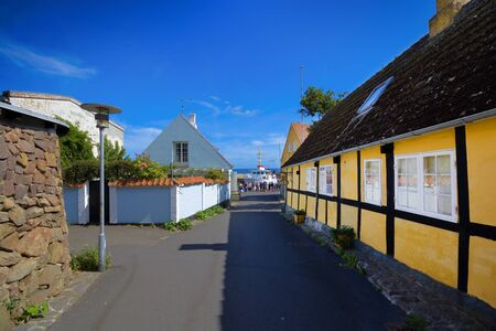 GUDHJEM, DENMARK - AUGUST 21, 2018: Traditional colorful half-timbered houses in the street leading towards harbor. Ship moored in the harbor in the background.のeditorial素材