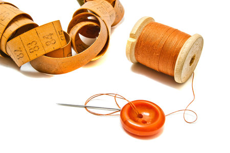 orange spool of thread, meter and button on white