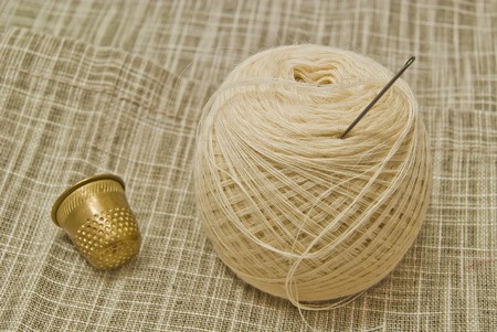 white yarn with needle and thimble on fabricの写真素材