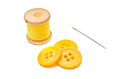 buttons and spool of yellow thread closeup on white