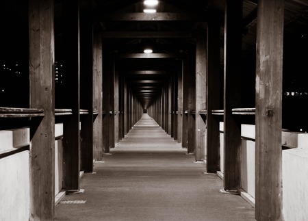 long wooden tunnel lit by lamps black and whiteの写真素材