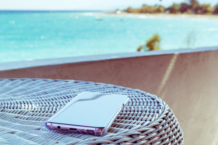 Mobile phone on a table. Sea in the horizontal holiday background