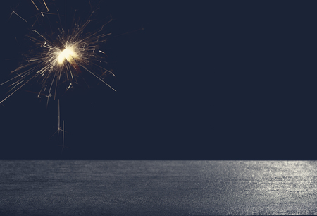 Dark background with festive yellow sparkler in front of empty stone concrete table for a celebration cardの写真素材