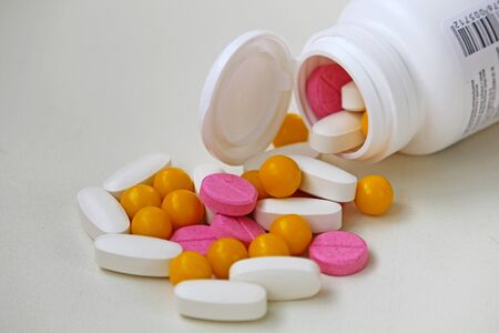 White, yellow and rose tablets pills poured from jar on white backgroundの写真素材