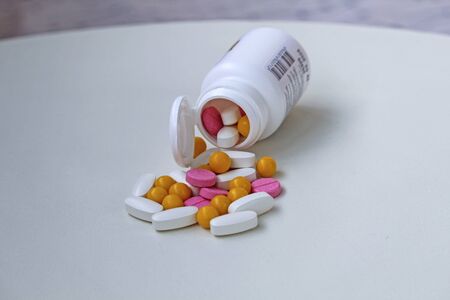 White, yellow and rose tablets pills poured from jar on white backgroundの写真素材