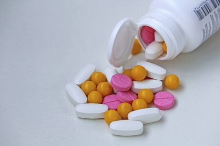 White, yellow and rose tablets pills poured from jar on white backgroundの写真素材