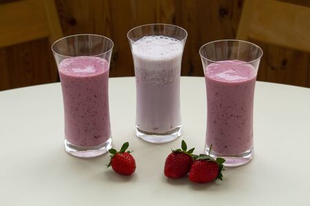 Three glasses of strawberry smoothie milkshake with strawberry on white tableの写真素材