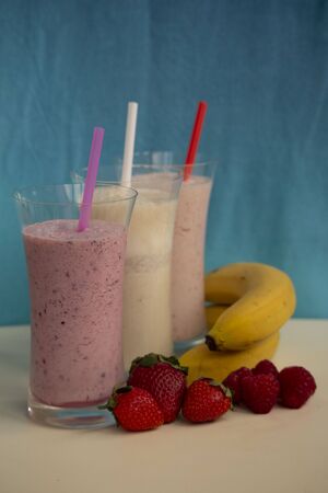 fresh fruit smoothie milkshake with berries and bananas blue backgroundの写真素材