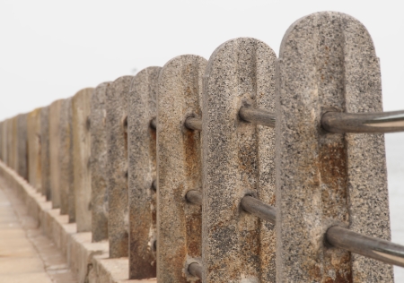 Cement stanchions connected by stainless steel rails to create a barrier separating a sidewalk from a riverの写真素材