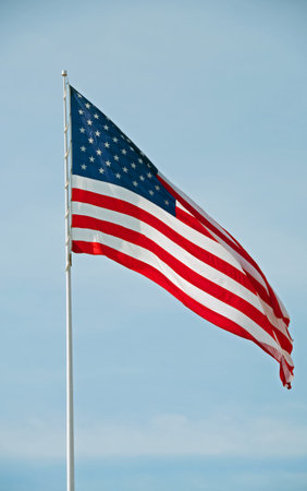A photograph of the United States flag flying from a flagpole against a bright blue sky