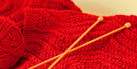 A photo of a hand-knitted red scarf with yarn and knitting needlesの写真素材