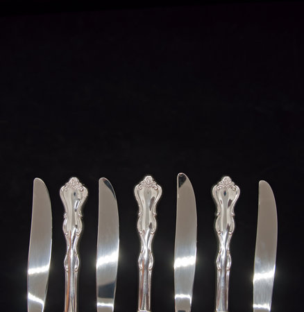 A photographic bottom border of seven sterling silver knives showing four blades and three handles on a black backgroundの写真素材