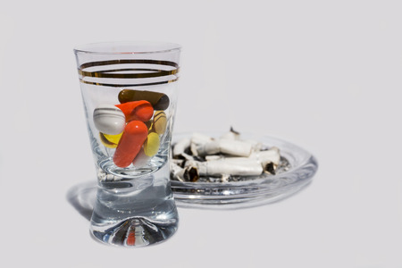 Pills in glass and cigarette buttsの写真素材