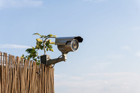 CCTV security camera on garden fence with blue sky in background - horizontal image