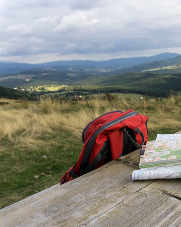 Wooden bench with hiking maps and backpack. Mountain landscape in background, nobody. Silesian Beskids, Poland.の写真素材