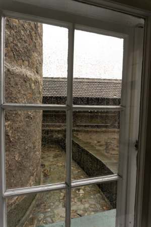Old window of medieval castle with wooden frame. Thick wall. Rain drops on glass. View from inside.