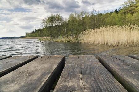 Wooden platform on the lake overlooking the shore of the lake on a cloudy day. Real photo. Selective focus.の写真素材
