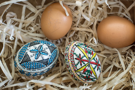Two decorated easter eggs and two fresh organic eggs on strawの写真素材