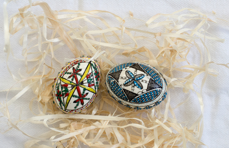 Two traditional handmade  Easter eggs in straw on white cloth. Traditional pattern from Bucovinaの写真素材