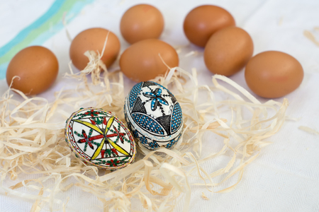 Traditional handmade  Easter eggs in straw on white cloth and few organic fresh eggs in background. Traditional pattern from Bucovinaの写真素材