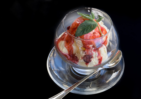 Vanilla ice cream with strawberries, fruit glaze and mint leaves in a glass bowl on a black background. Copy space.
の写真素材