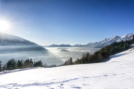 Winter mountain landscape. Blue sky with bright sun, fog in the valley. Tirol, Alps, Austria.の写真素材