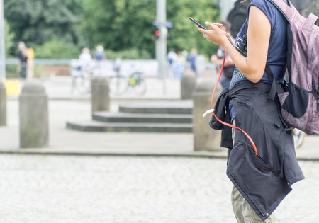 Young tourist girl using mobile smartphone searching location while travelling, on vacations. Smartphone is connected by red cable with powerbank in pocket of her jacket.
の写真素材