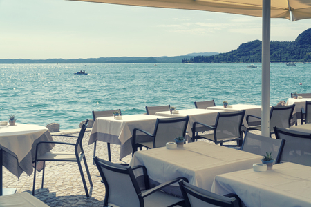 Cafe on the edge of the sea or lake, tables covered with white tablecloths with ashtrays and decorative pots on a sunny summer day, standing in the shade of an umbrellaの写真素材