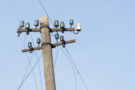 Old electric  wooden pole with glass and ceramic insulators and electric wires against blue sky. Copy space.の写真素材