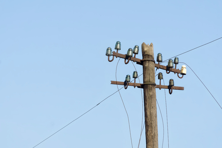 Old electric  wooden pole with glass and ceramic insulators and electric wires against blue sky. Copy space.の写真素材