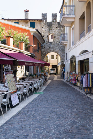 BARDOLINO, VENETO REGION, ITALY - AUGUST 7, 2017:restaurant and shops on the street in Bardolino near the San Giovanni Gate.のeditorial素材