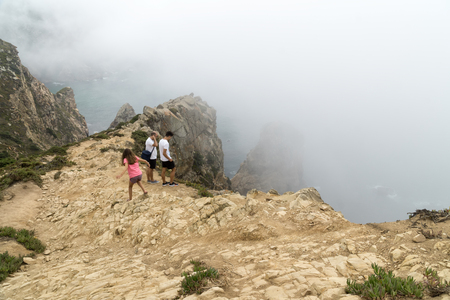 CABO DA ROCA, PORTUGAL - September 2 2018: Tourists on Cape Roca cliffs in fog. The rocks are obscured by clouds or fog. Cape Roca is most western part of Europe.のeditorial素材