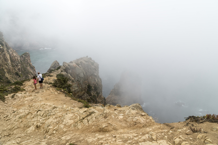 CABO DA ROCA, PORTUGAL - September 2 2018: Tourists on Cape Roca cliffs in fog. The rocks are obscured by clouds or fog. Cape Roca is most western part of Europe.のeditorial素材