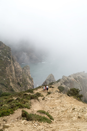 CABO DA ROCA, PORTUGAL - September 2 2018: Tourists on Cape Roca cliffs in fog. The rocks are obscured by clouds or fog. Cape Roca is most western part of Europe.のeditorial素材