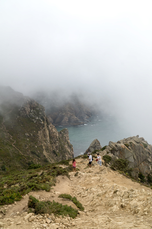 CABO DA ROCA, PORTUGAL - September 2 2018: Tourists on Cape Roca cliffs in fog. The rocks are obscured by clouds or fog. Cape Roca is most western part of Europe.のeditorial素材