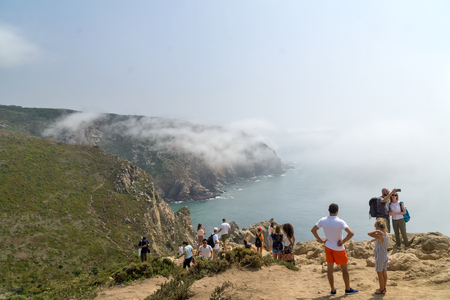 CABO DA ROCA, PORTUGAL - September 2 2018: Tourists on Cape Roca cliffs in fog. The rocks are obscured by clouds or fog. Cape Roca is most western part of Europe.のeditorial素材