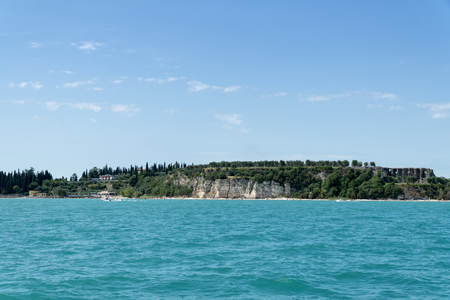 Stony Beach of Sirmione town on Garda Lake with view of Grottoes of Catullus (Grotte di Catullo), the ruins of a Roman villa built at the end of the 1st century B.C. View from Garda Lake.の写真素材