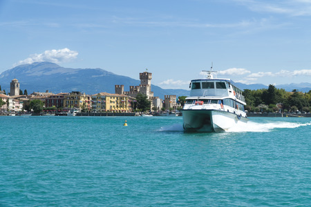 Sirmione, Italy -  August 07 2017: Tourist ship on Lake Garda. Panorama of Sirmione, Caligero Castle and mountains in the background.のeditorial素材
