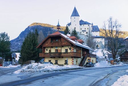 MAUTERNDORF, AUSTRIA, JANUARY 21. 2020: Castle in Mauterndorf with a traditional wooden house in the foreground in winter. Horizontal image.のeditorial素材