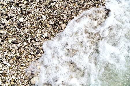 Colorful pebbles on the beach partly covered with foamed water. Abstract background with copy space.の写真素材