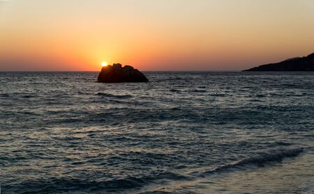Breathtaking sunset over the wavy sea  with a rock in front, red glow in the sky.  Horizontal image.の写真素材