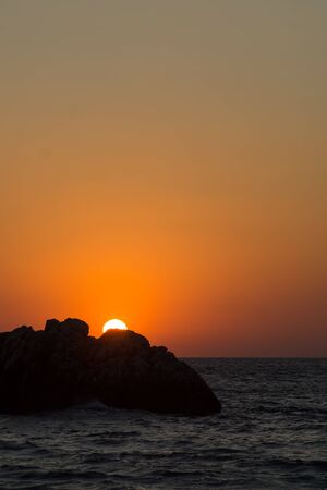 Breathtaking sunset over the wavy sea  with a rock in front, red glow in the sky. Vertical image.の写真素材