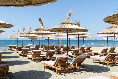 The rows of empty sunbeds with straw umbrellas on the beach. Blue sky and turquoise sea. Sunny summer day. Vlora / Vlore, Albania, Europe.の写真素材
