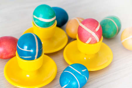 Colorful painted homemade easter eggs with modern pattern on yellow coasters on wooden table. Easter decoration, easter background.の写真素材