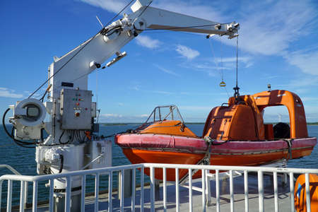 Orange lifeboat, rescue boat of ferry boat sailing on the sea with blue sky and coastline in the background.の写真素材