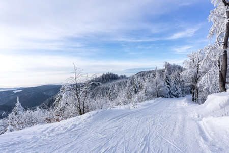 Winter mountain landscape. Trail to cross-country skiing on a mountain road, trees covered with hoarfrost and snow, blue sky with white clouds. Kremnica Mountains, Slovakia.の写真素材