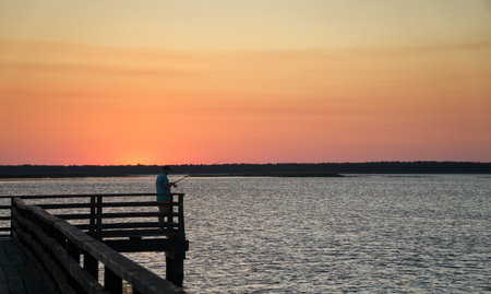 Angler silhouette on the pier at sunset in summer at Lebsko Lake, Pomerania, Poland, Europe.の写真素材